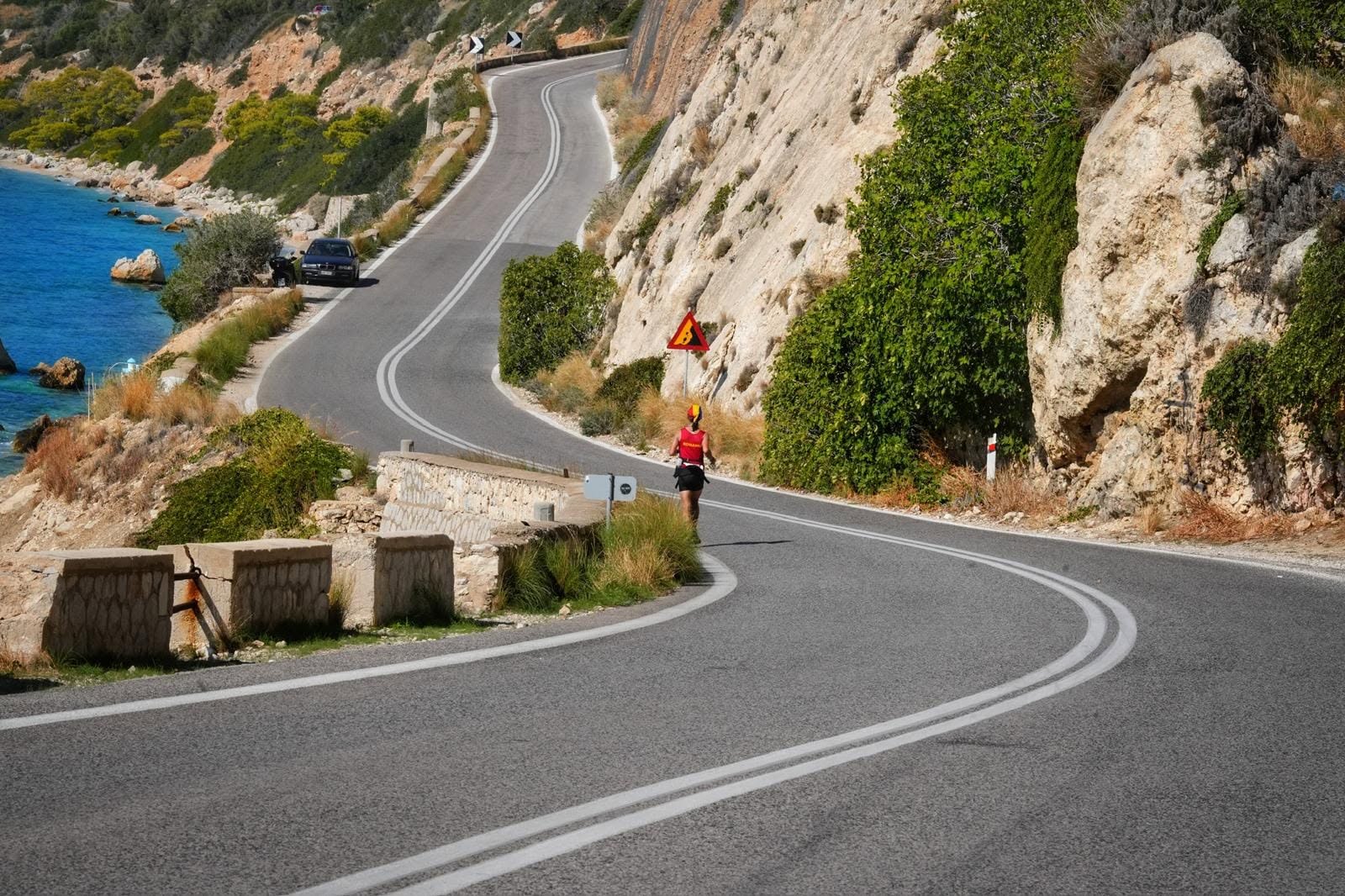 A runner following a winding cliffside road beside the sea