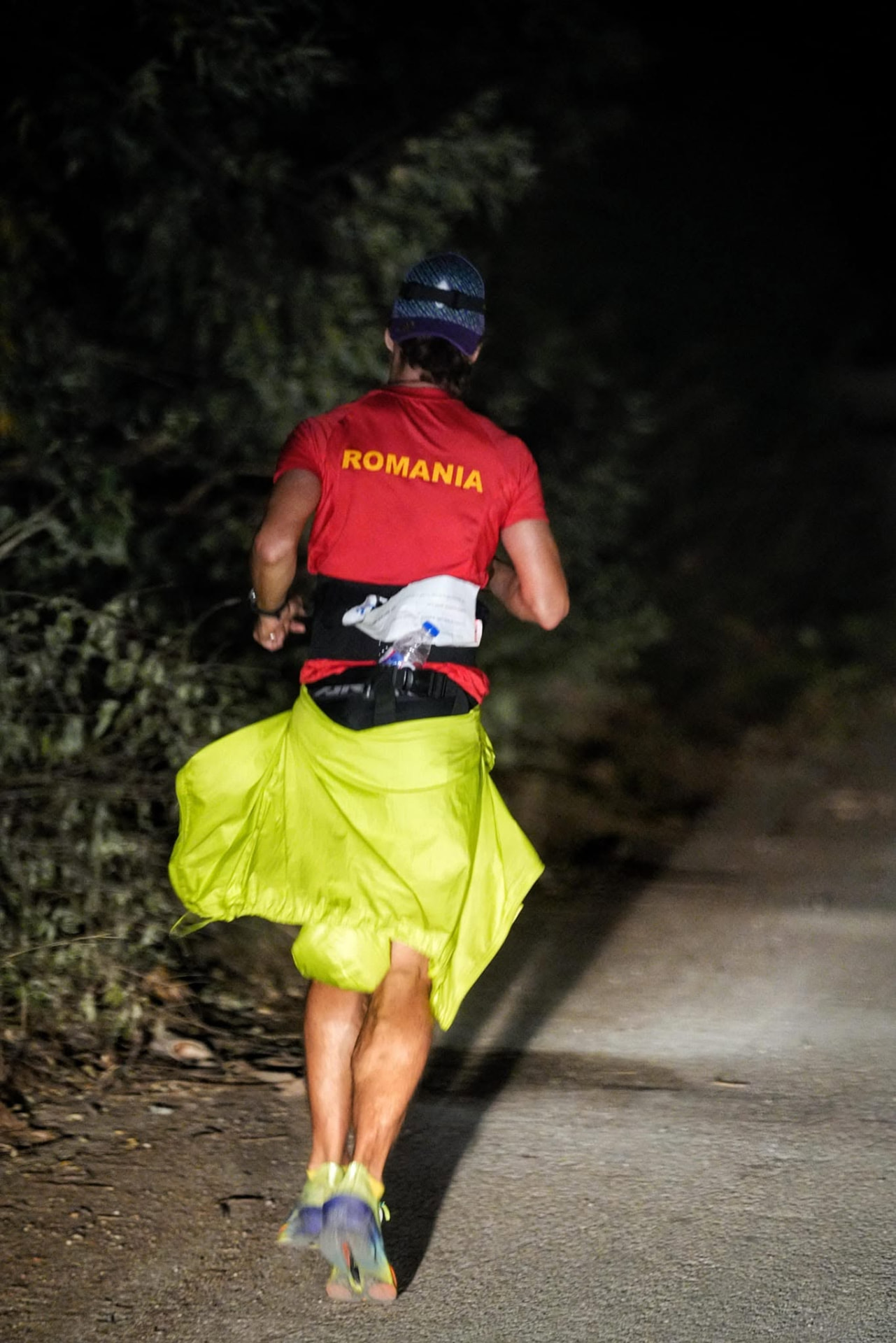 A runner in a red Romania shirt running on a dark trail at night