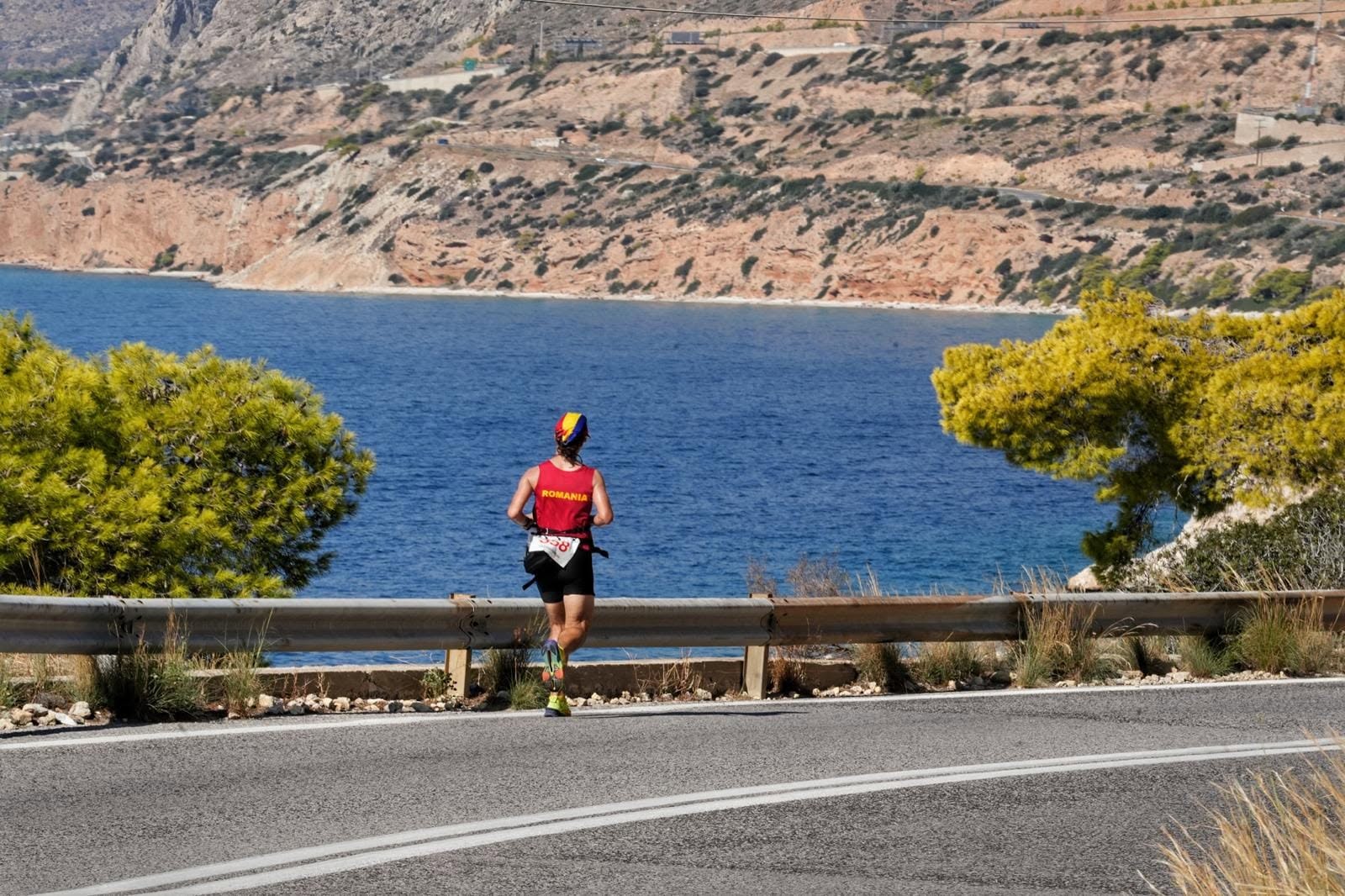 A runner in a red Romania vest running along a coastal road above the sea